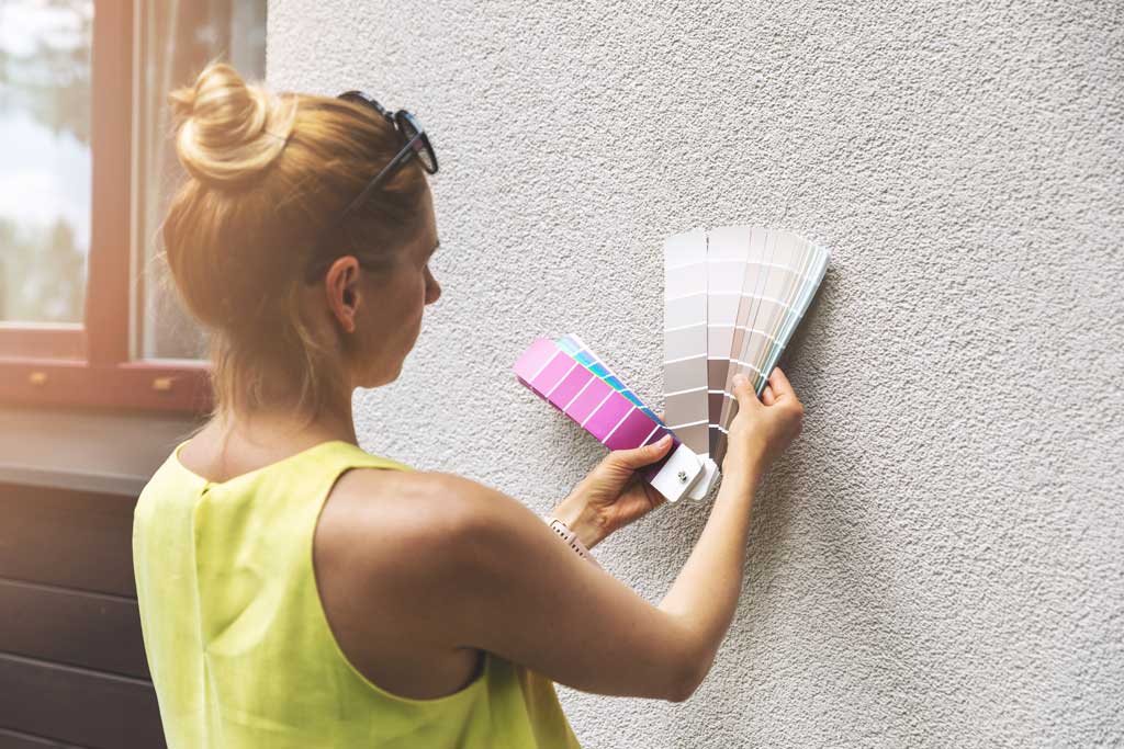 Image of a woman looking at paint color swatches on the exterior of her home